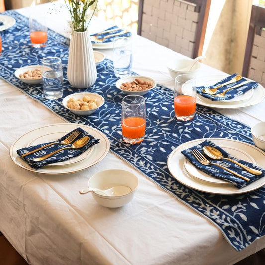 Dining table set with blue and white patterned tablecloth, plates, glasses, and cutlery.