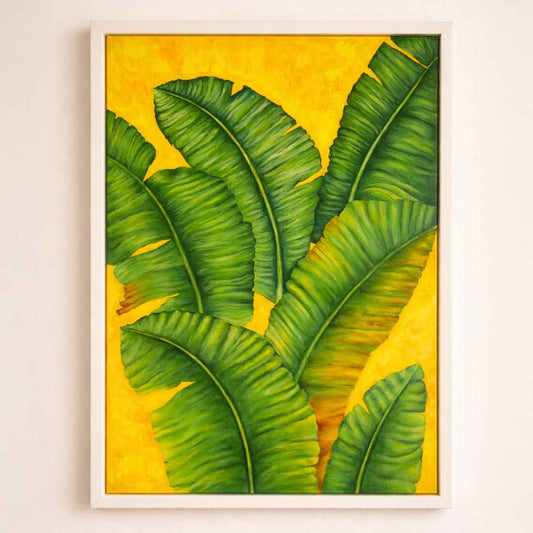 Framed artwork of green leaves on a yellow background on a white wall.