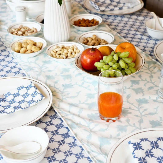 Table setting with fruit, nuts, and a glass of juice on a patterned tablecloth, table runner and napkins