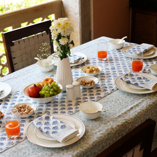 Dining table set with plates, glasses, and a vase of flowers on a patterned tablecloth, table runner and napkins