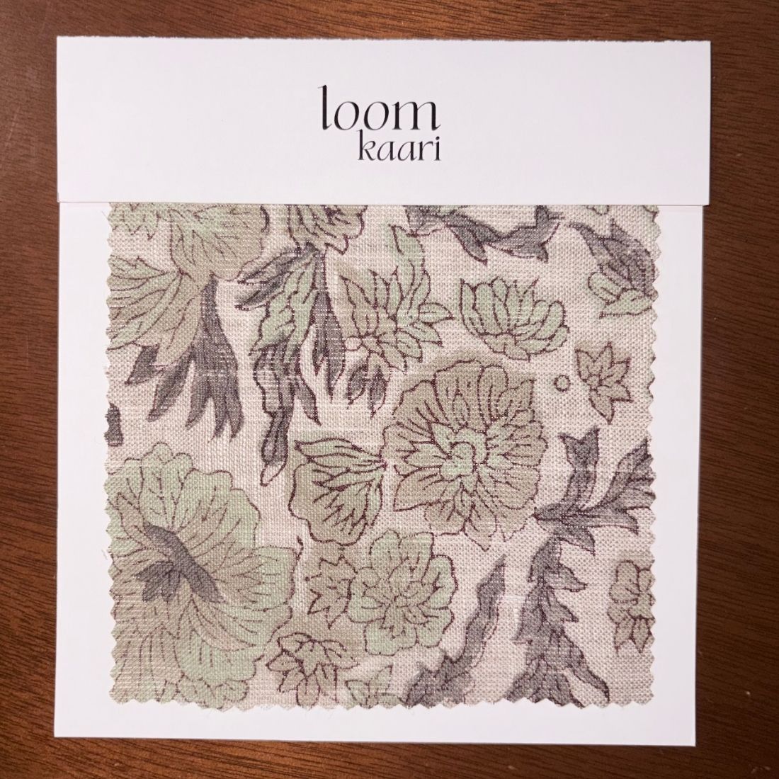 Floral patterned fabric swatch on a white card with 'loom kaari' branding, on a wooden surface.