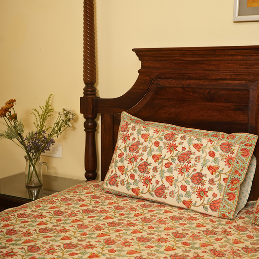 Floral-patterned bedspread and pillow on a wooden bed with a side table and flowers.