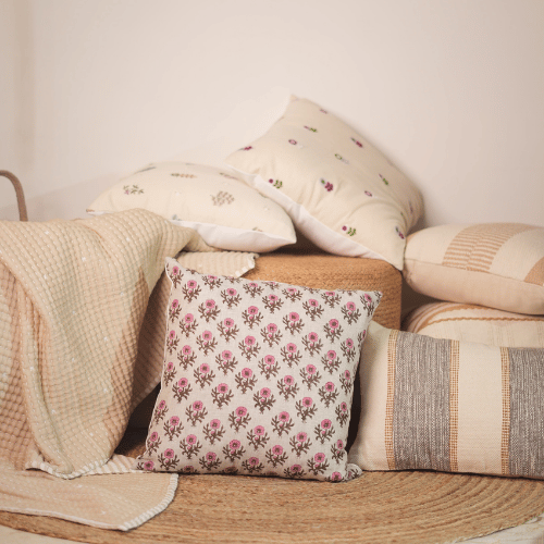 Collection of patterned pillows and a blanket on a wooden surface with a neutral background