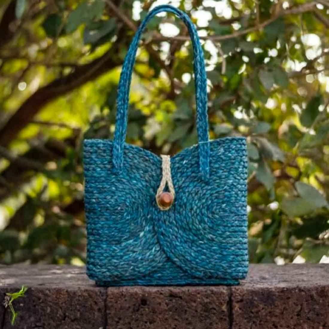 Blue woven handbag on a stone ledge with green foliage in the background