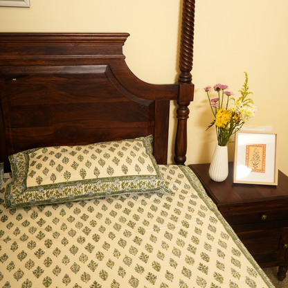 Bed with patterned bedding and pillows, nightstand with flowers and picture frame.