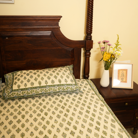 Bed with patterned bedding and pillows, nightstand with flowers and picture frame.