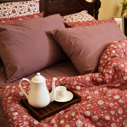 Tray with teapot and cup on a bed with floral bedding and pillows.