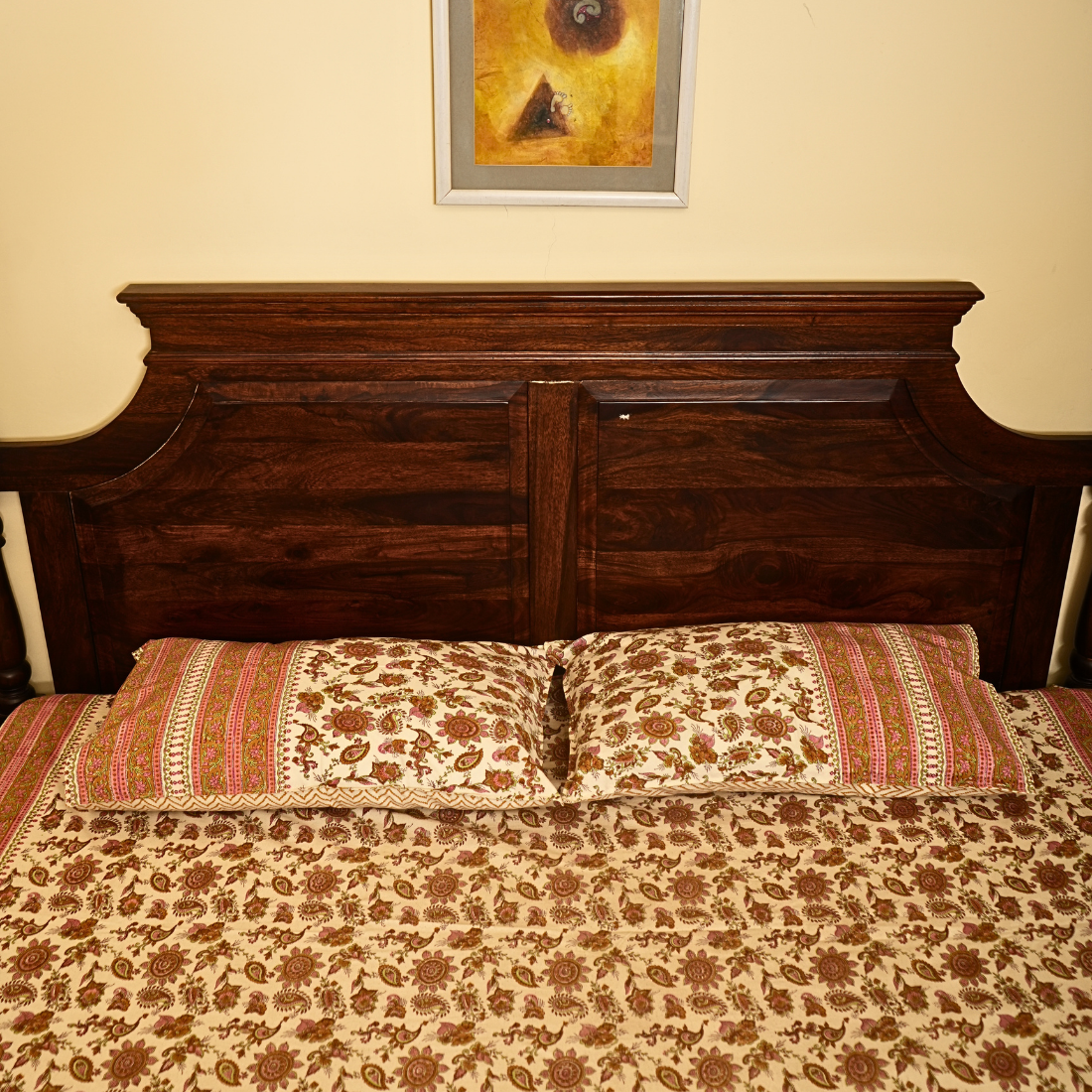 Wooden headboard with floral bedding and pillows in a bedroom setting.