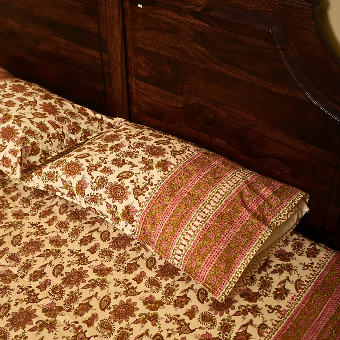 Floral patterned bedspread with decorative pillow on a wooden bed frame.