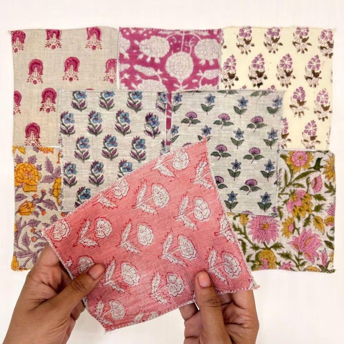 A person's hands hold a pink and white patterned fabric square in front of a grid of nine other colorful patterned fabric squares on a white background.