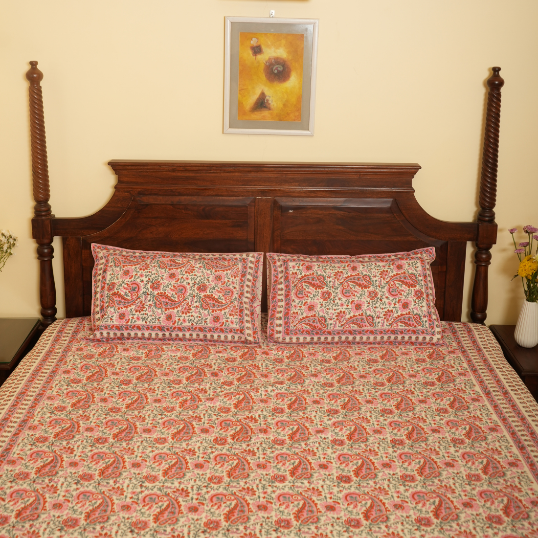 Bed with floral bedding and wooden headboard against a beige wall with a framed picture.