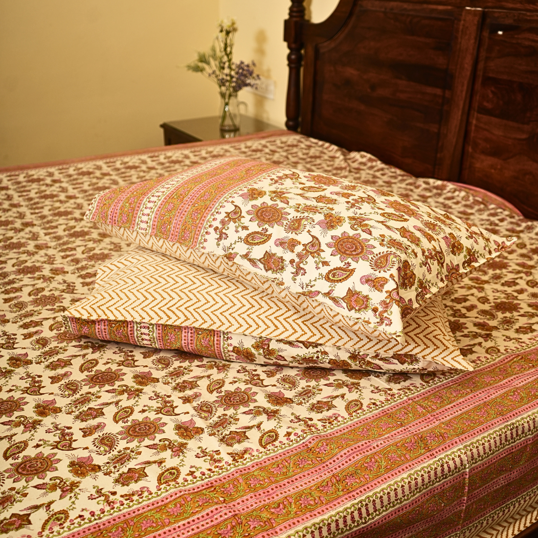 Patterned bedspread and pillows on a bed with a wooden headboard.