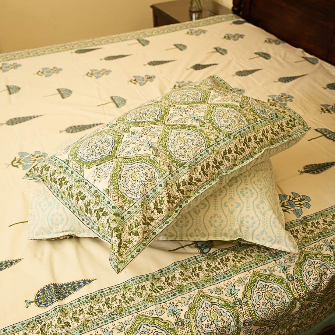 Decorative pillows with green and beige pattern on a matching bedspread.