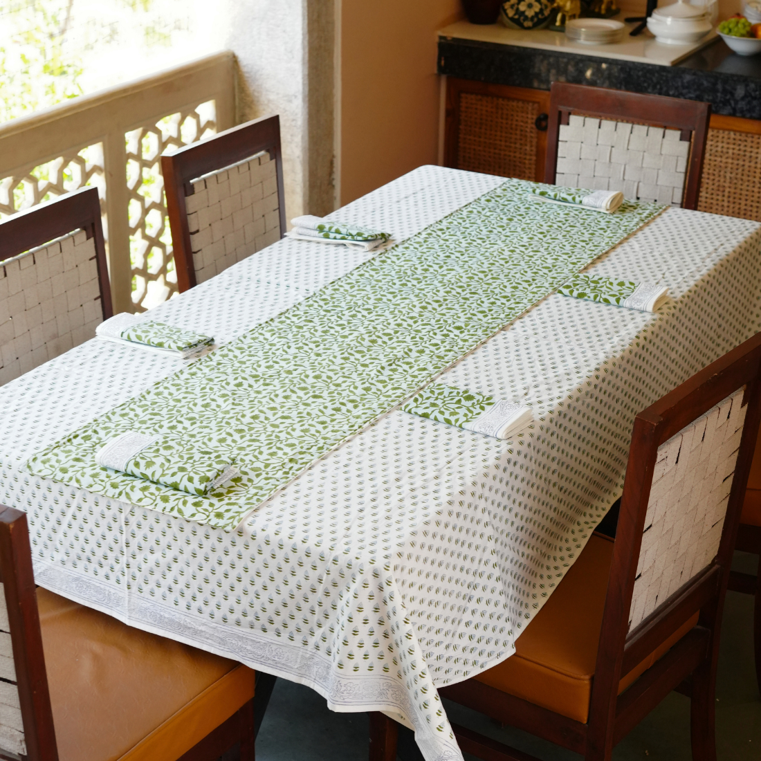 Dining table with a green and white jaal tablecloth and chairs.