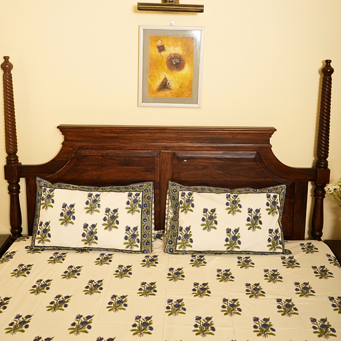 Floral patterned bedspread on a wooden bed with a decorative pillow and framed artwork on the wall.