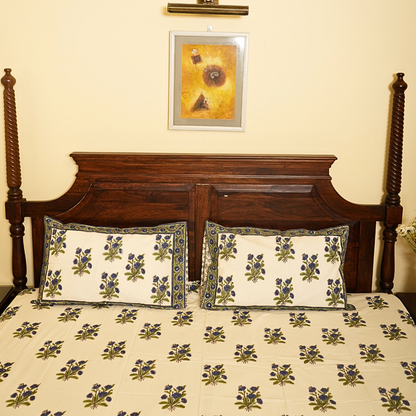 Floral patterned bedspread on a wooden bed with a decorative pillow and framed artwork on the wall.