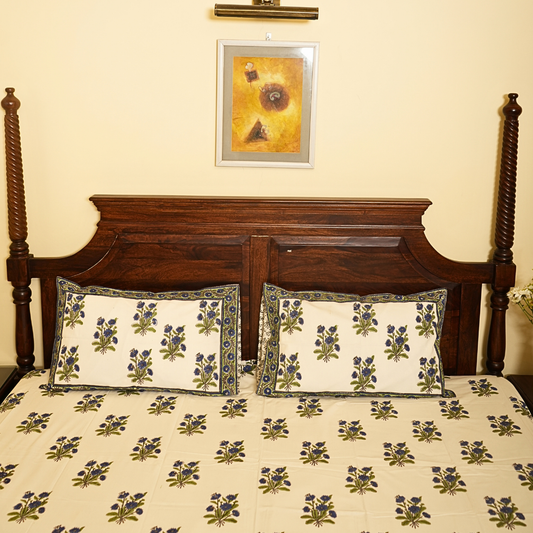 Floral patterned bedspread on a wooden bed with a decorative pillow and framed artwork on the wall.