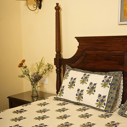 Bed with floral patterned bedding and pillow, nightstand with flowers, wooden headboard.