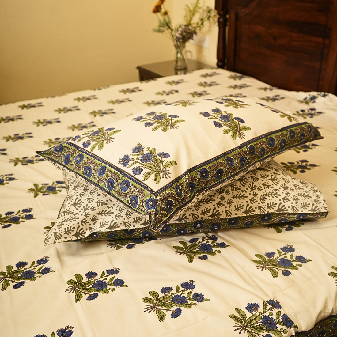 Floral patterned bedspread and pillows on a bed with a wooden headboard.