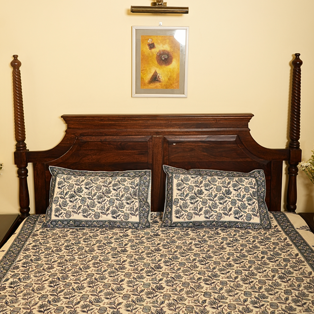 Bed with floral bedding and pillows, wooden headboard, and framed picture on wall.