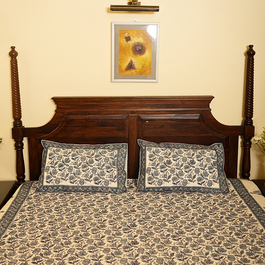 Bed with floral bedding and pillows, wooden headboard, and framed picture on wall.