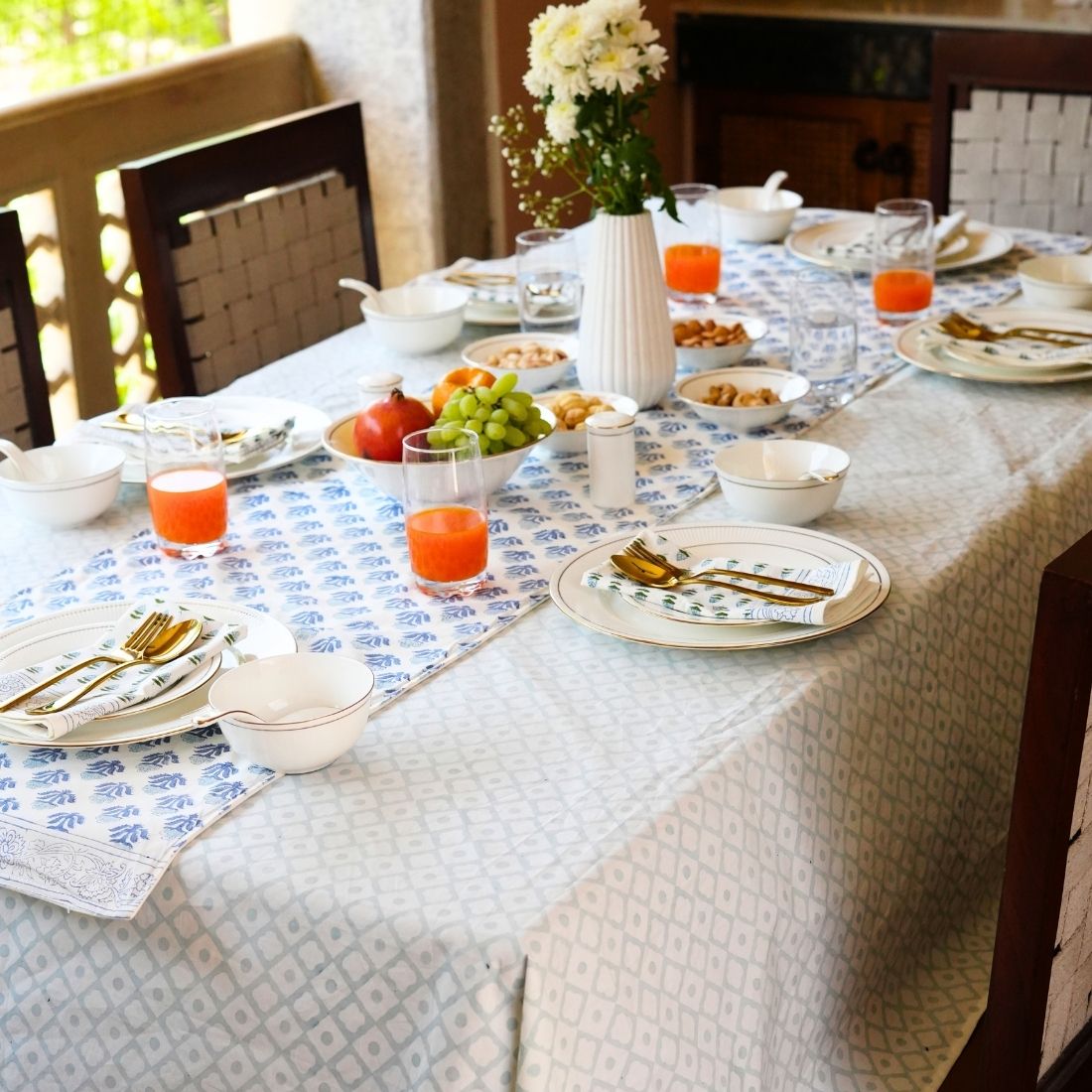 Dining table styled with a blue and white tablecloth, table runner, napkins, plates, bowls, and cutlery.