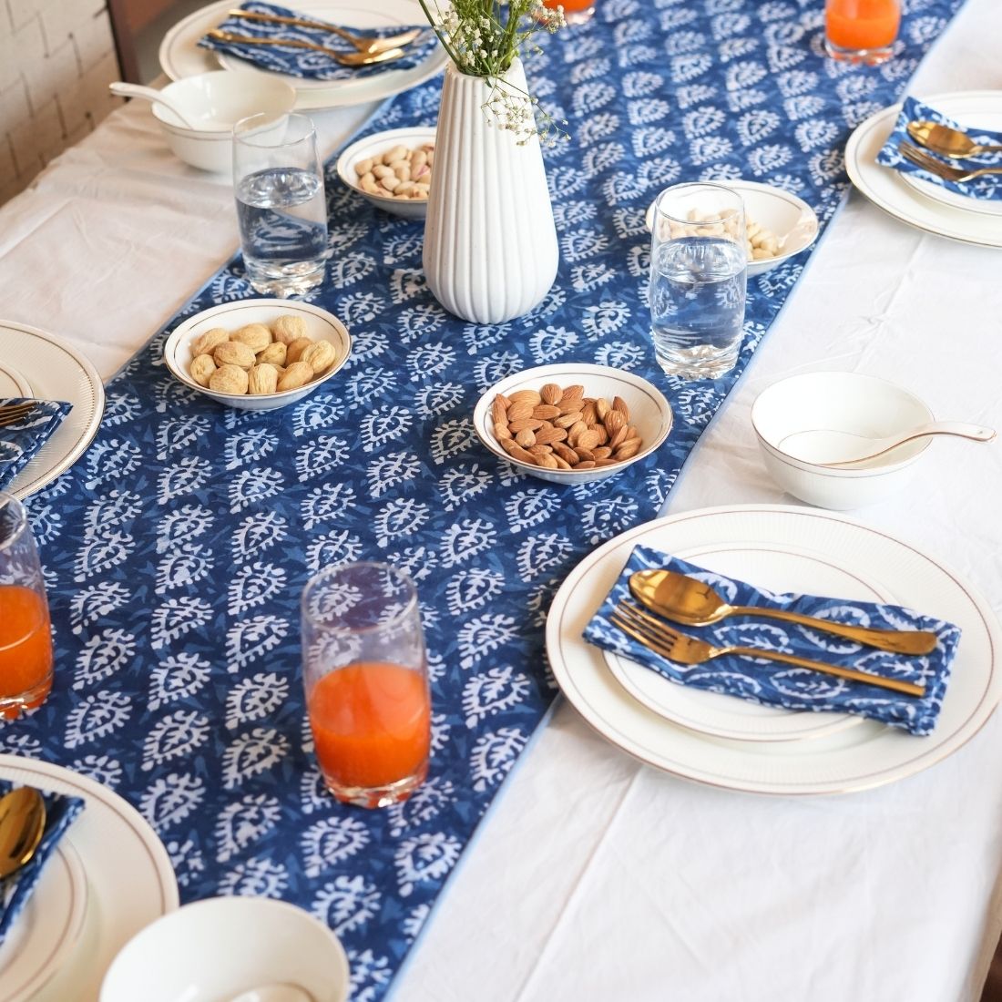 Dining table set with blue and white patterned tablecloth, plates, glasses, and bowls.