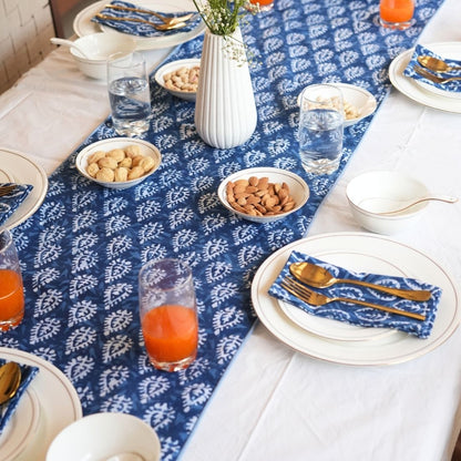 Dining table set with blue and white patterned tablecloth, plates, glasses, and bowls.