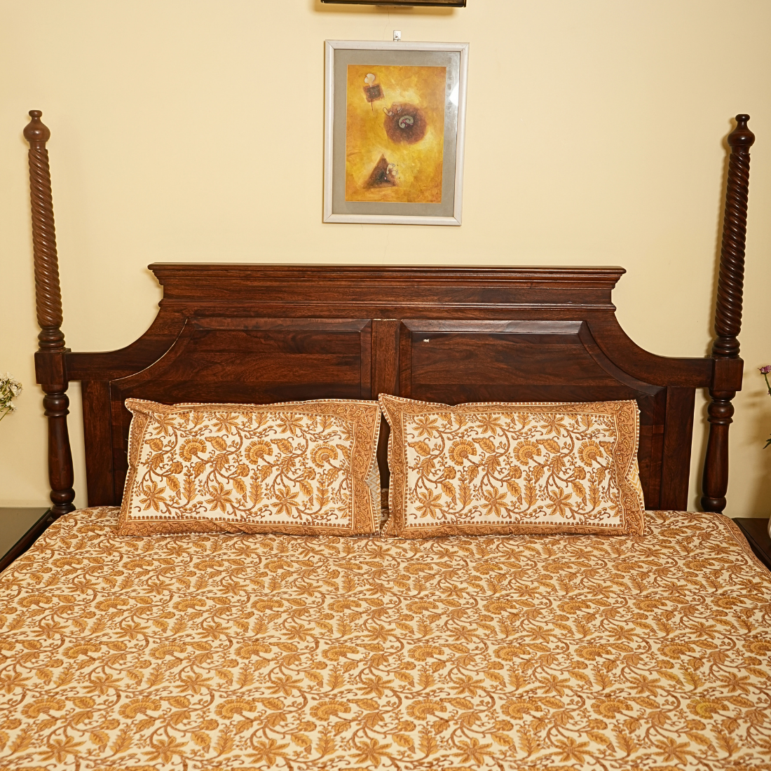 Bed with wooden headboard and floral bedding, framed artwork on wall.