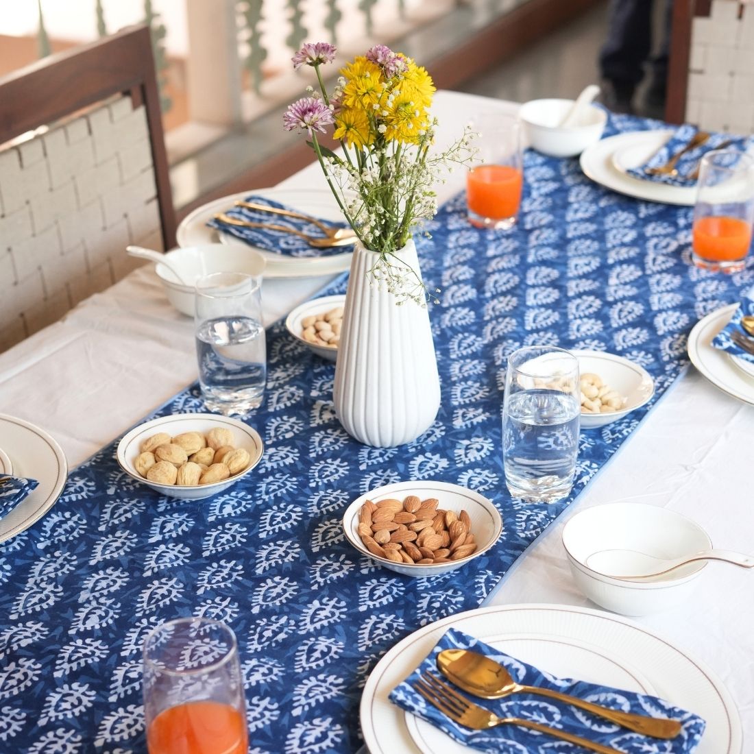 Table setting with blue and white patterned tablecloth, plates, bowls, and a vase with flowers.