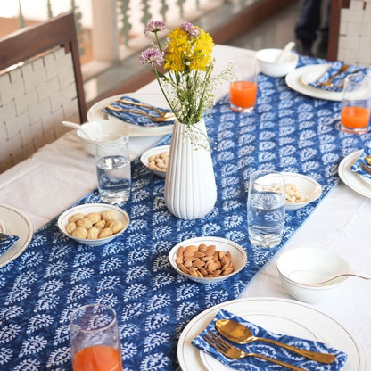 Table setting with blue and white patterned tablecloth, plates, bowls, and a vase with flowers.