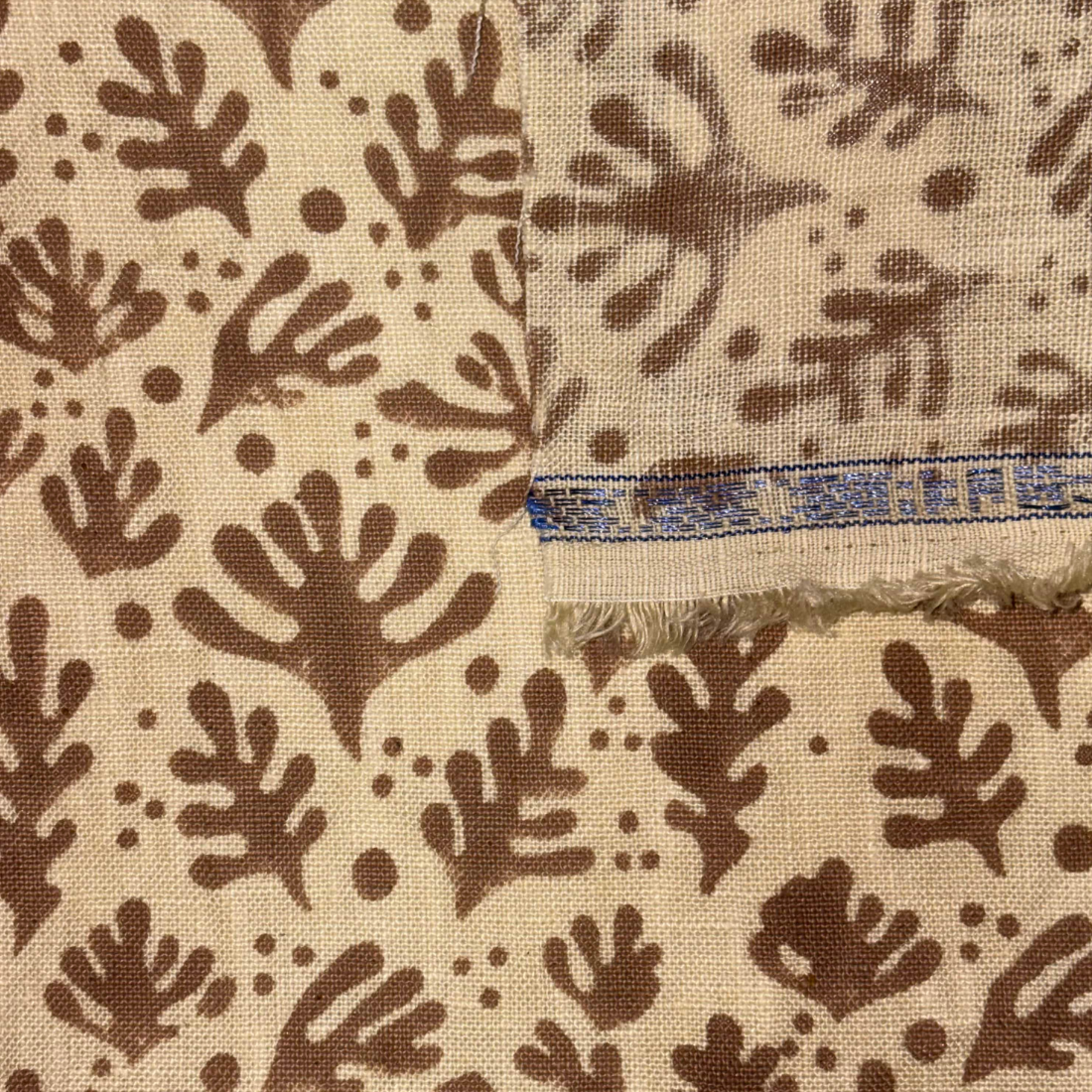 Textile with brown leaf pattern on beige background, showing a brand label.