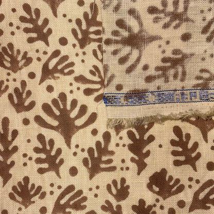 Textile with brown leaf pattern on beige background, showing a brand label.