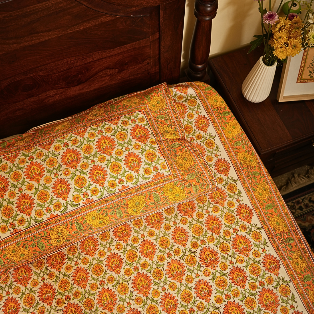 Decorative floral-patterned bedsheet with a vase of flowers in the background.
