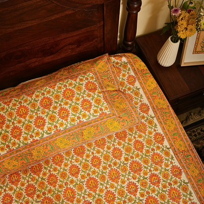 Decorative floral-patterned bedsheet with a vase of flowers in the background.