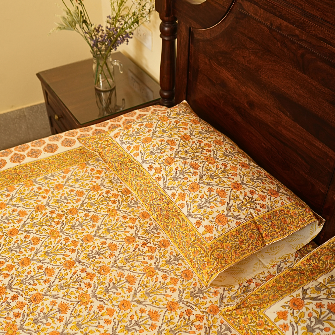 Floral patterned bedspread on a wooden bed with a side table in the background.