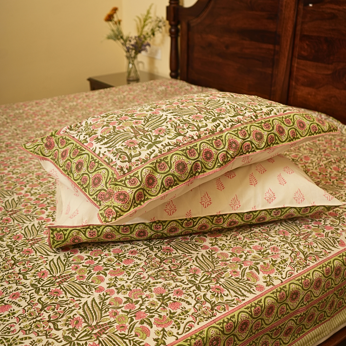 Floral patterned pillows on a matching bedspread with a wooden headboard.