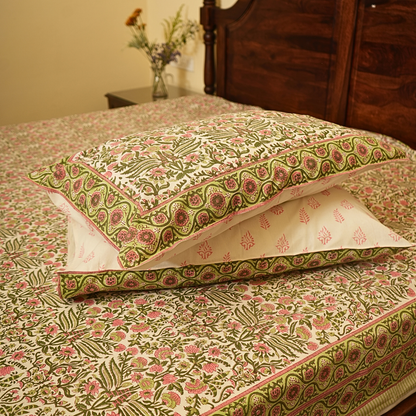 Floral patterned pillows on a matching bedspread with a wooden headboard.