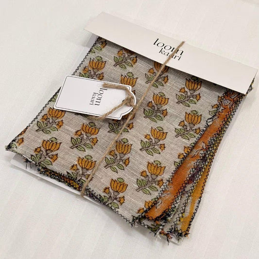 A swatch set with a beige and brown floral pattern and orange accents, shown with its white paper packaging tag on a white background.