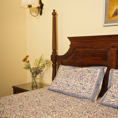 Bedroom with floral bedspread and pillows, nightstand with flowers, and wall sconce.