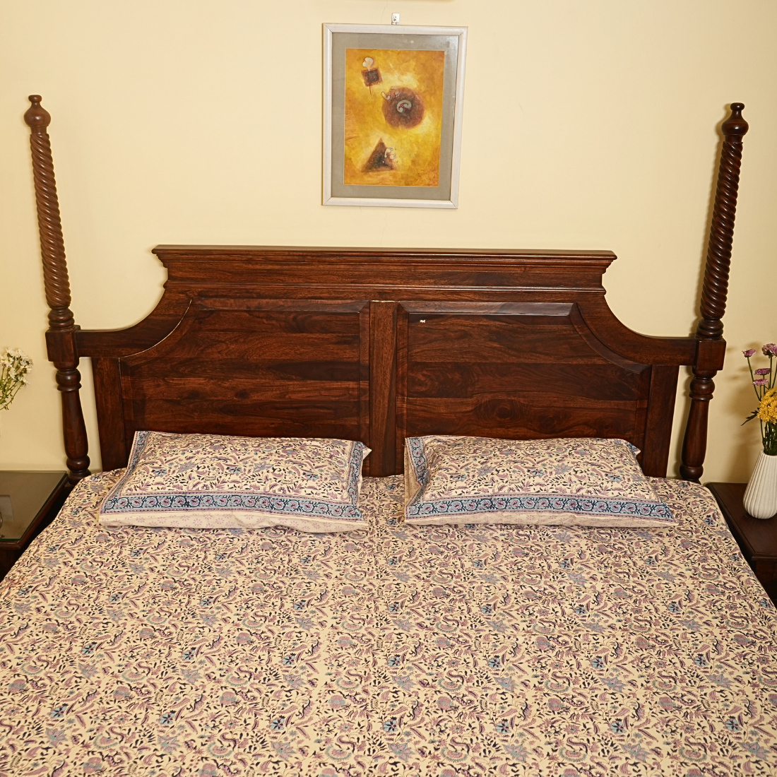 Wooden bed with floral bedding and a framed picture on the wall.