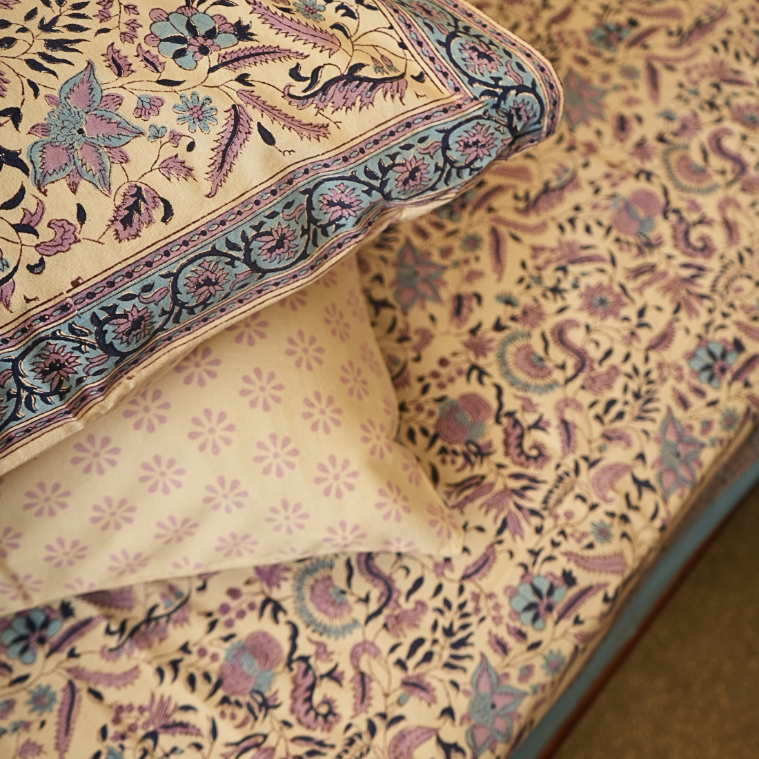 Close-up of patterned bedsheet and pillows with floral and paisley designs on a beige background