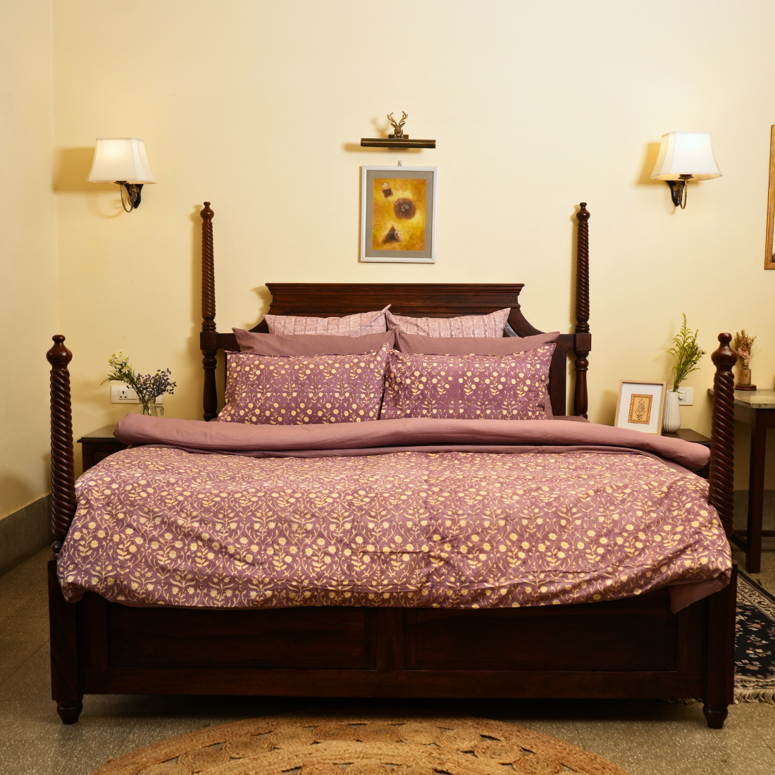 Bedroom with a wooden bed and purple floral bedding, wall art, and lamps.