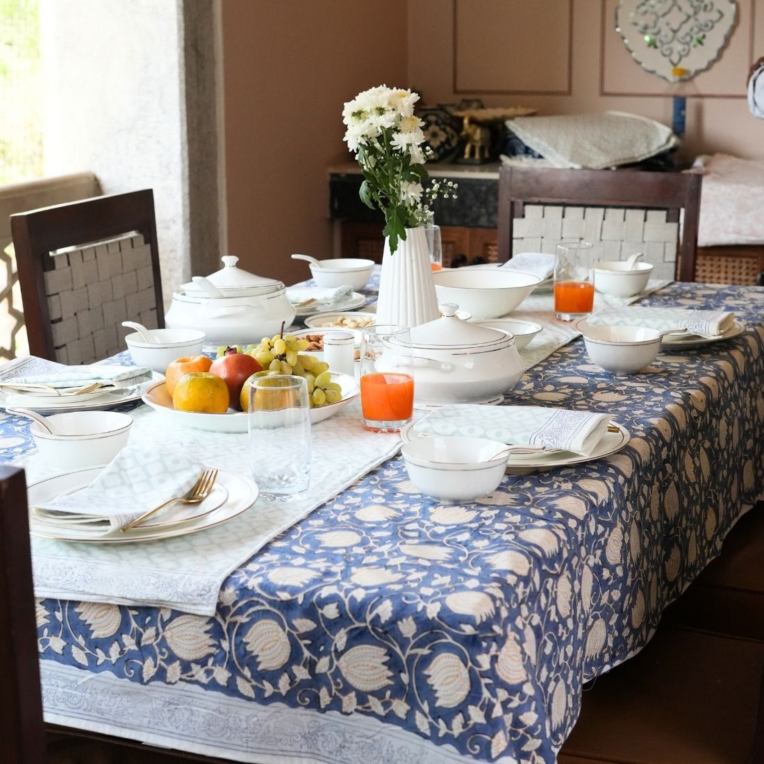 Dining table styled with a blue and white patterned tablecloth, table runner, napkins, plates, bowls, and cutlery.