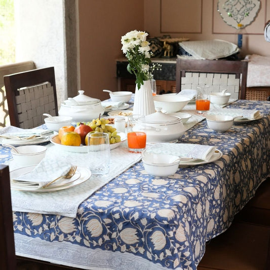Dining table styled with a blue and white patterned tablecloth, table runner, napkins, plates, bowls, and cutlery.