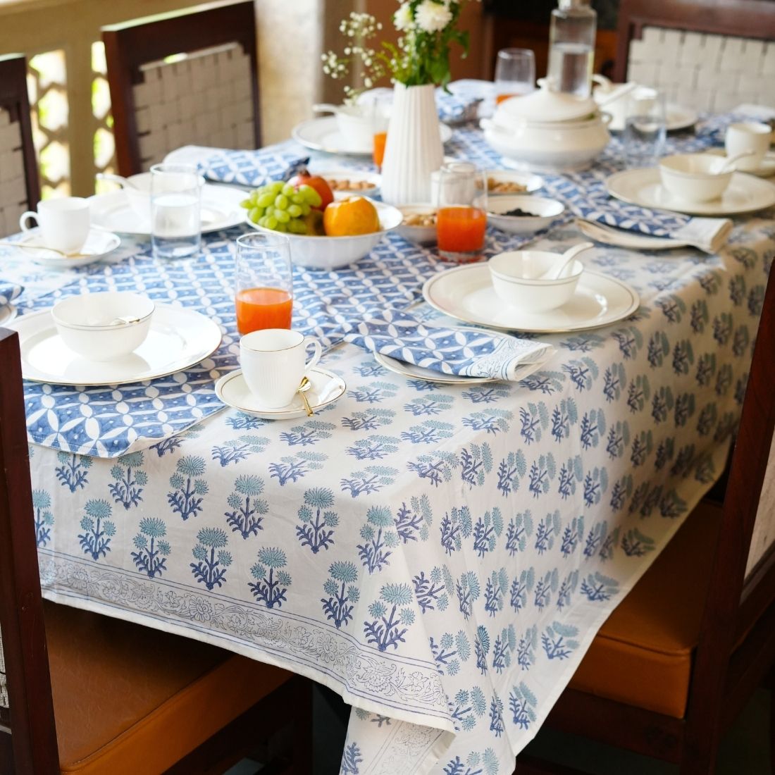 Dining table styled with a blue and white patterned tablecloth, table runner, napkins, plates, bowls, and cutlery.