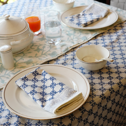 Dining table setting with plates, glasses, and a teapot on a patterned tablecloth.