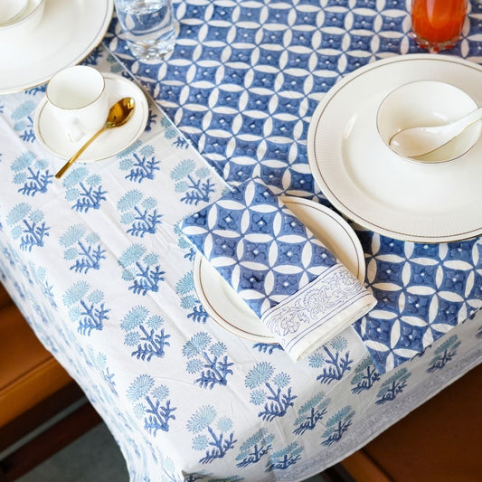 Table setting with blue and white patterned tablecloth, table runner , napkins, white plates, and silverware.