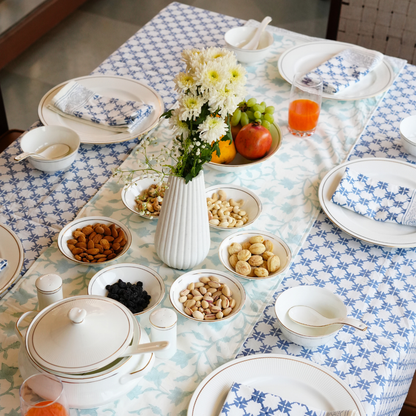 Dining table set with plates, bowls, and snacks on a blue and white checkered tablecloth.