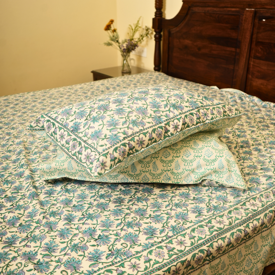 Floral patterned bedspread on a bed with a wooden headboard.
